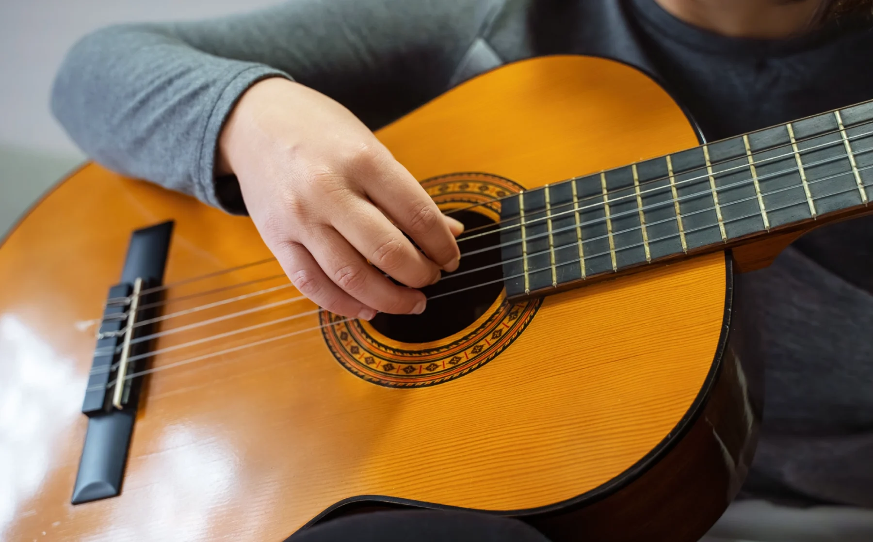 Person playing an acoustic guitar with fingers on strings.