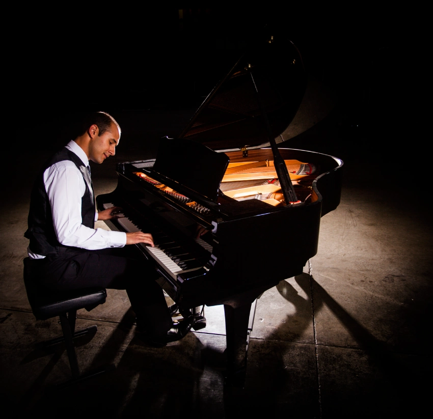 Man in formalwear playing a grand piano on stage.